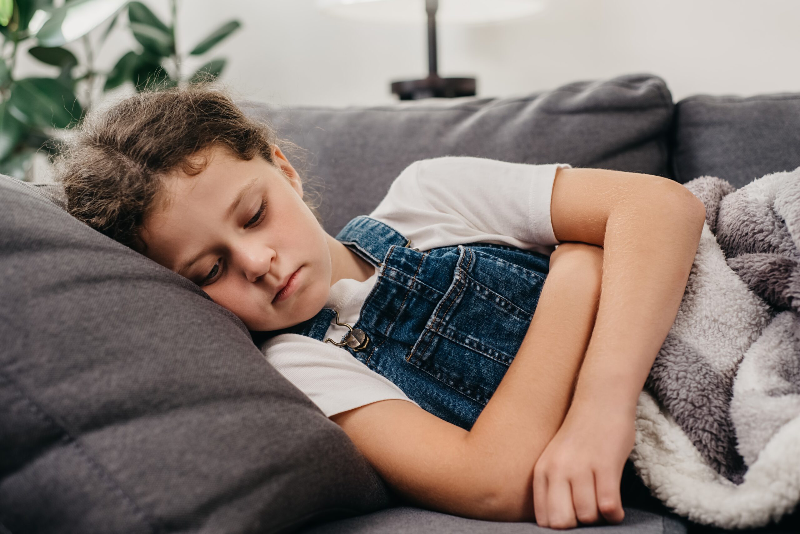 A child resting on a couch with a blanket, appearing tired or unwell during a winter illness.