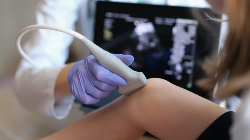 Doctor performing ultrasound examination on child's knee joint with handheld transducer probe
