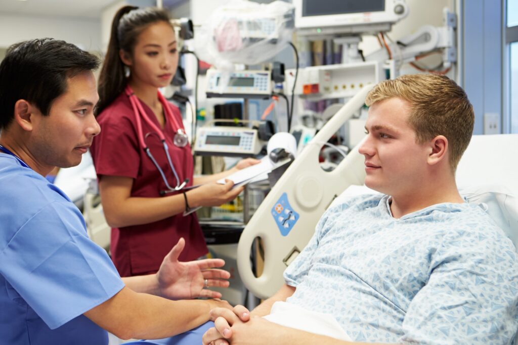 Male patient in hospital gown speaking with two medical professionals in white coats in an emergency room setting