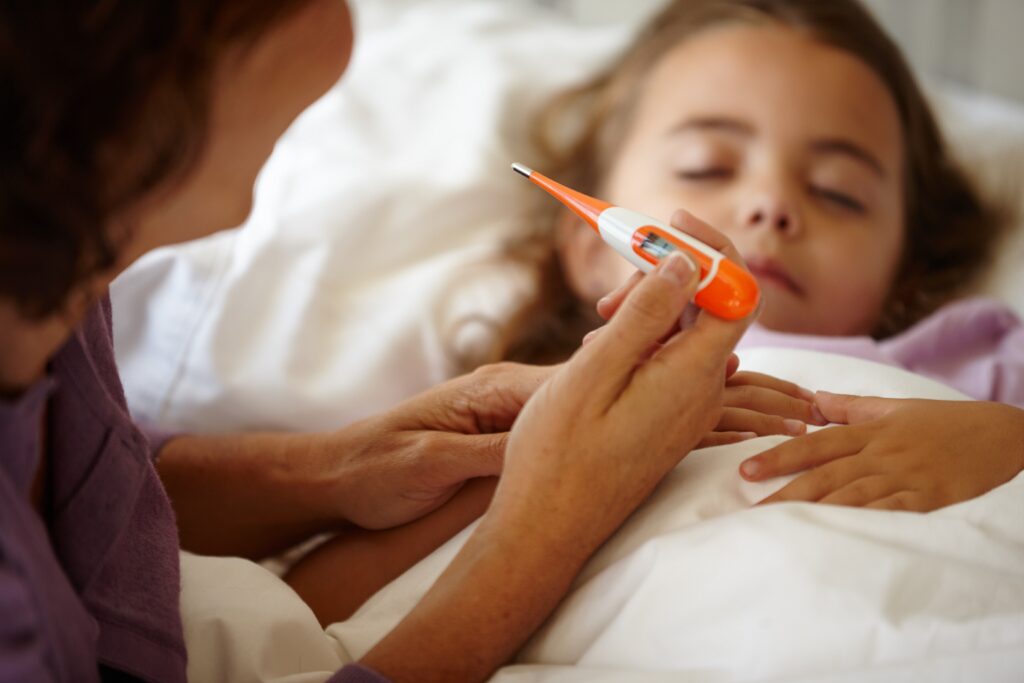 Mother checking thermometer while caring for sick child resting in bed.