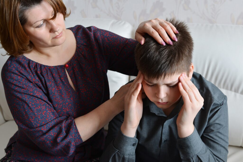Mother placing hand on head of young boy with a headache, holding head in hands.